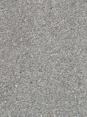 A detailed, full-frame macro shot of a gray asphalt or concrete surface with a rough, granular texture and pebbles.