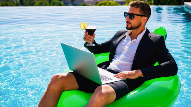 A businessman in a comfortable black suit, wearing glasses, sitting on a green inflatable ring in a swimming pool. He has a laptop on his lap and holds a drink in his right hand.