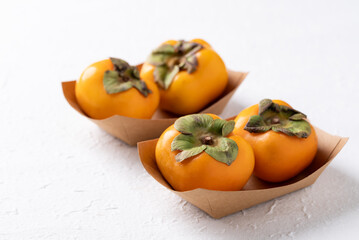 Fresh ripe persimmon in kraft paper bowl on white background, Autumn sweet fruit
