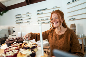 Small business owner serving muffins in cafe with positive attitude