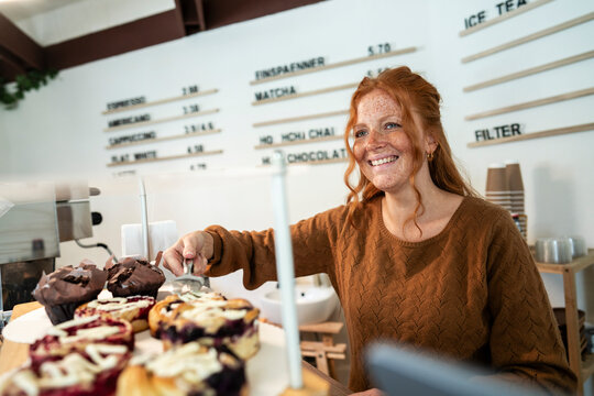 Small business owner serving muffins in cafe with positive attitude
