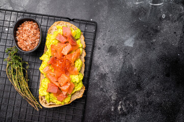 Toast with salty salmon, trout slices, avocado and red caviar. black background. top view