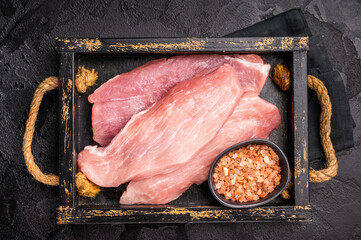 Raw pork chop fillet steaks in a wooden tray. black background. top view