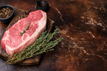 Raw New York strip beef steak, also named Striploin steak on a wooden board. brown background. top...