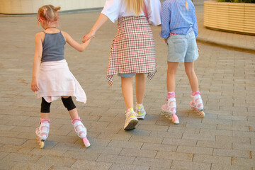 Joyful family moment: mother holding hands with two girls skating outdoors during sunset in city...