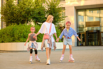 Mother and her two daughters roller skating outdoors in city park at sunset, holding hands and...