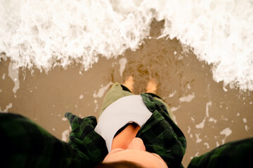Aerial perspective of bare female feet standing where waves meet sand. Ideal for beach holiday and...