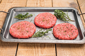 Raw hamburger minced meat patties  for burgers with herbs on tray. wooden background. top view