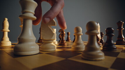 Hand directing ivory chess across grid with rival troops closeup. Strategic game