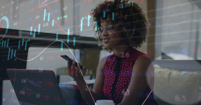 Woman wearing red blouse analyzing charts on laptop in living room, smartphone, coffee cup