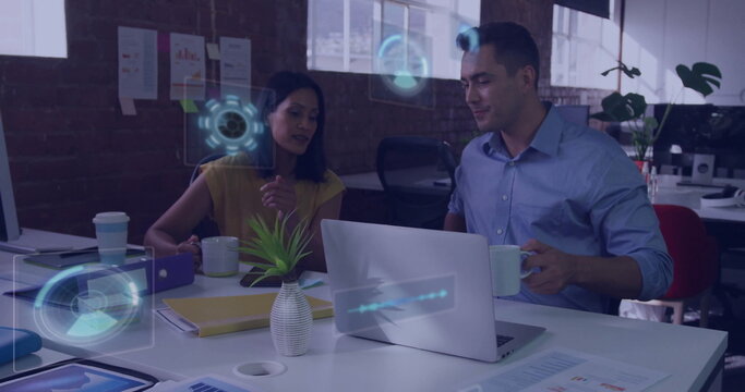 Collaborating colleagues in business attire examining charts at office desk, with laptop and mugs