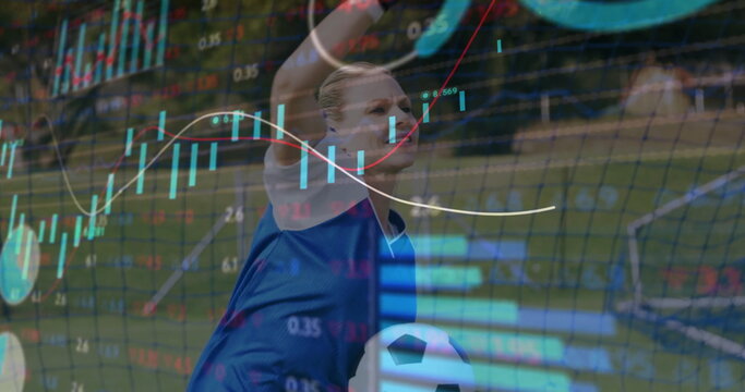 Raising arms goalkeeper in blue jersey catching ball on turf, financial charts overlaying net
