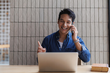 Asian freelancer talking on phone and pointing at laptop screen
