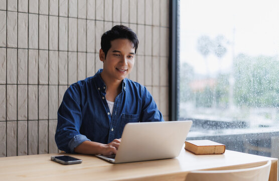 Young asian freelancer working on laptop in cozy cafe during rain