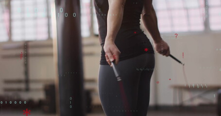 Jumping athlete wearing workout outfit skipping with jump rope in gym, with punching bag