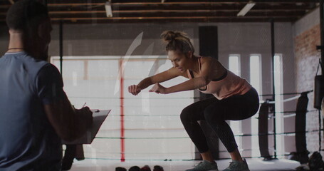 Trainee in sportswear performing squat jump onto step in boxing ring, trainer holding clipboard