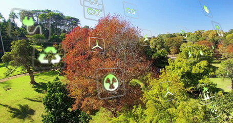 Floating icons of recycling, CO2 labels, wind turbine, radiation above park lawn, with wooden bench