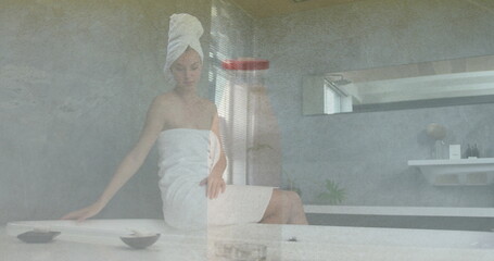 Sitting spa guest adjusting towel turban on head at spa bathroom marble bench, with shallow bowls