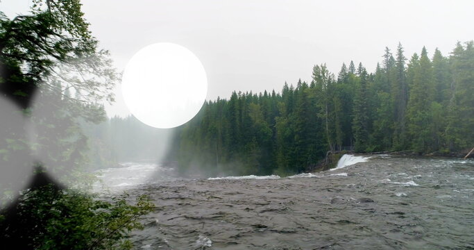 Fototapeta Flowing river rapids and waterfall coursing through tall evergreen trees, with mist and lens flare