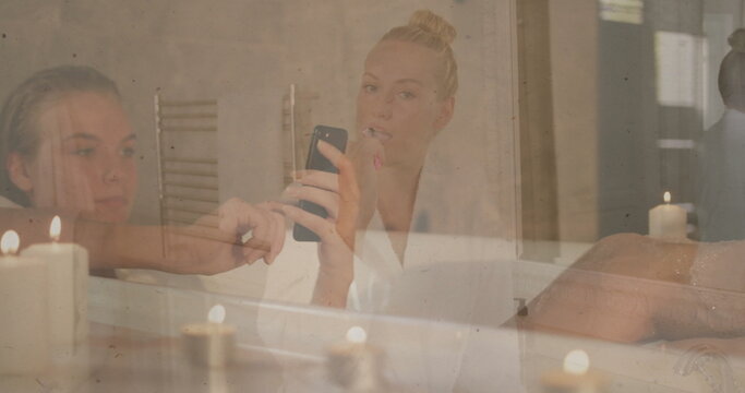Brushing teeth bathrobe woman holding toothbrush as friend checking smartphone at bathroom mirror