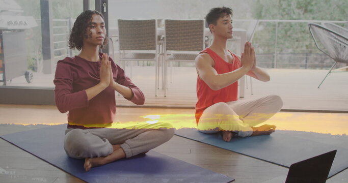 Meditating yoga partners wearing activewear on blue mats in home studio, with laptop, patio grill