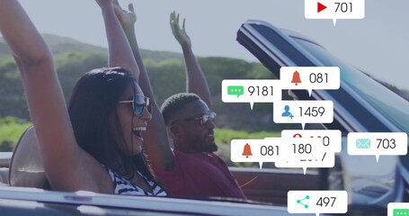 Driving couple in convertible raising arms through hills, with sunglasses, notification icons