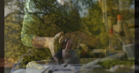 Shaping potter crafting small clay cup on spinning wheel in workshop, with double-exposure foliage