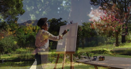 Painting African American woman applying green paint on canvas in lush garden, with lily pond