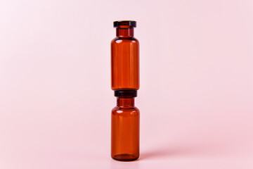 Two amber glass vials are stacked on top of each other against a light pink background....