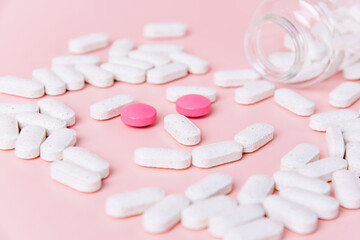 White and pink pills are scattered on a pastel pink surface with an overturned glass bottle. Concepts of health, wellness, and pharmaceutical product
