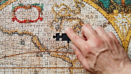 Closeup hand placing puzzle piece in vintage world map. Historical landscape