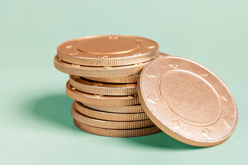 Stack of golden casino coins with card suits symbols on a light green background. Conceptual image for gambling and betting