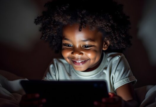 A dark-skinned boy plays a tablet in the dark