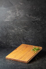Empty cutting board with rosemary on a black stone background.