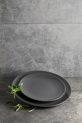 Empty round black plates with rosemary on a grey stone background.