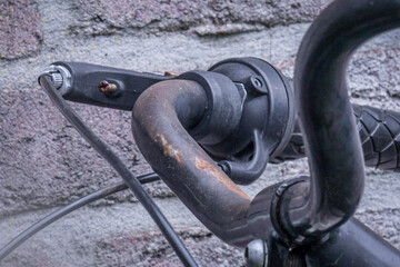Rusty bicycle handlebar close-up against a textured brick wall highlighting wear and age of the bike