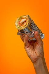 Hand holding bright juicy shawarma on orange background