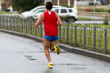 rear view runner running marathon on wet road, splashing mud on his legs