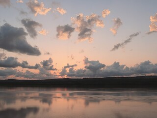 A serene view of a body of water reflecting the sky at sunset with clouds above it all