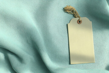 Elegant blank fabric tag with rope floating above soft light blue textile background, creating calm and minimalistic atmosphere for product display or branding concepts