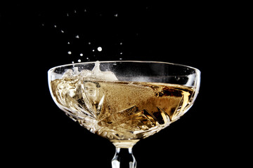 Elegant close-up of sparkling champagne in a classic coupe glass with dynamic splashes and effervescent bubbles against a dramatic black background, perfect for celebrations and luxury themes.