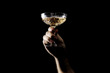 Hand holding a sparkling champagne coupe glass against a dark, dramatic black background, signifying celebration and luxury.