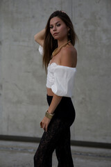 Fototapeta premium Stylish young woman in fashionable clothes posing confidently outdoors. Fashion model look with urban background, long hair, black shoes, and modern accessories.