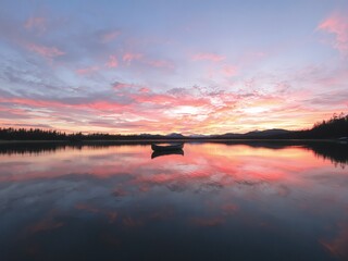 A serene lake reflecting a vibrant sunset with a small boat floating peacefully on water