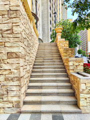 Obraz premium A set of stairs ascends to an elevated walkway that is beautifully framed by lush trees and modern buildings, all set against the backdrop of a bright, sunny day in a vibrant urban environment