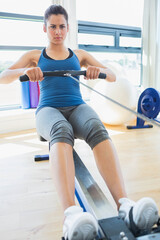 Fototapeta premium Woman pulling rowing handle on machine in fitness studio wearing blue tank top and gray leggings
