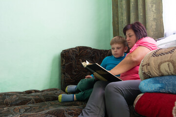 Obraz premium Cozy reading: A woman reads a book aloud to a boy on a couch, fostering a love for learning and creating a shared experience.