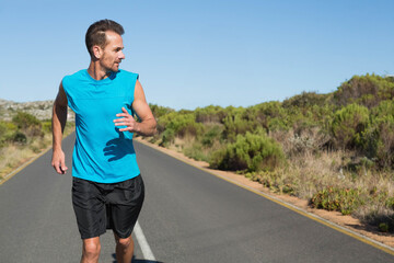 Mature adult man running along paved rural road with center line wearing turquoise athletic shirt