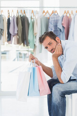 Man sitting on bench in bright clothing store holding pastel shopping bags, copy space
