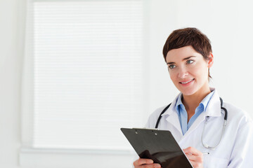 Female doctor holding black clipboard and stethoscope in clinic room wearing lab coat copy space